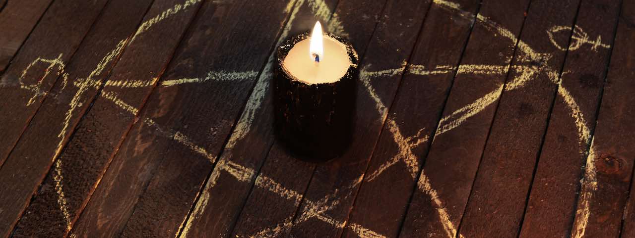 Eine brennende Kerze steht in der Mitte eines mit Kreide gezeichneten Pentagramm-Symbols.