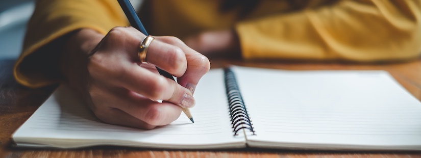 Eine frauenhand hält einen Bleistift über einem Notizbuch